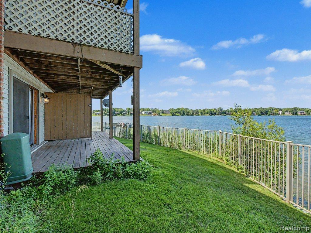 1974 Klingensmith Road, Unit 4 Bloomfield Hills, MI 48302 - Photo 24 of 35 Expansive lakefront setting featuring a wooden deck, sliding glass door access, a metal perimeter fence, and a vibrant blue sky