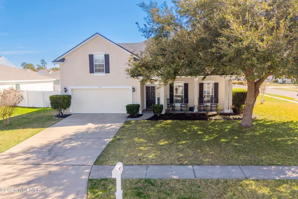 a view of a white house with large trees and plants