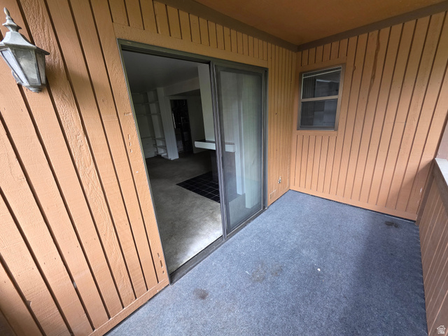 6852 Countrywoods Circle, Unit 5D Midvale, UT 84047 - Photo 12 of 50 Covered patio featuring outdoor carpeting, wood paneling, an exterior wall sconce, and sliding glass door access to the interior