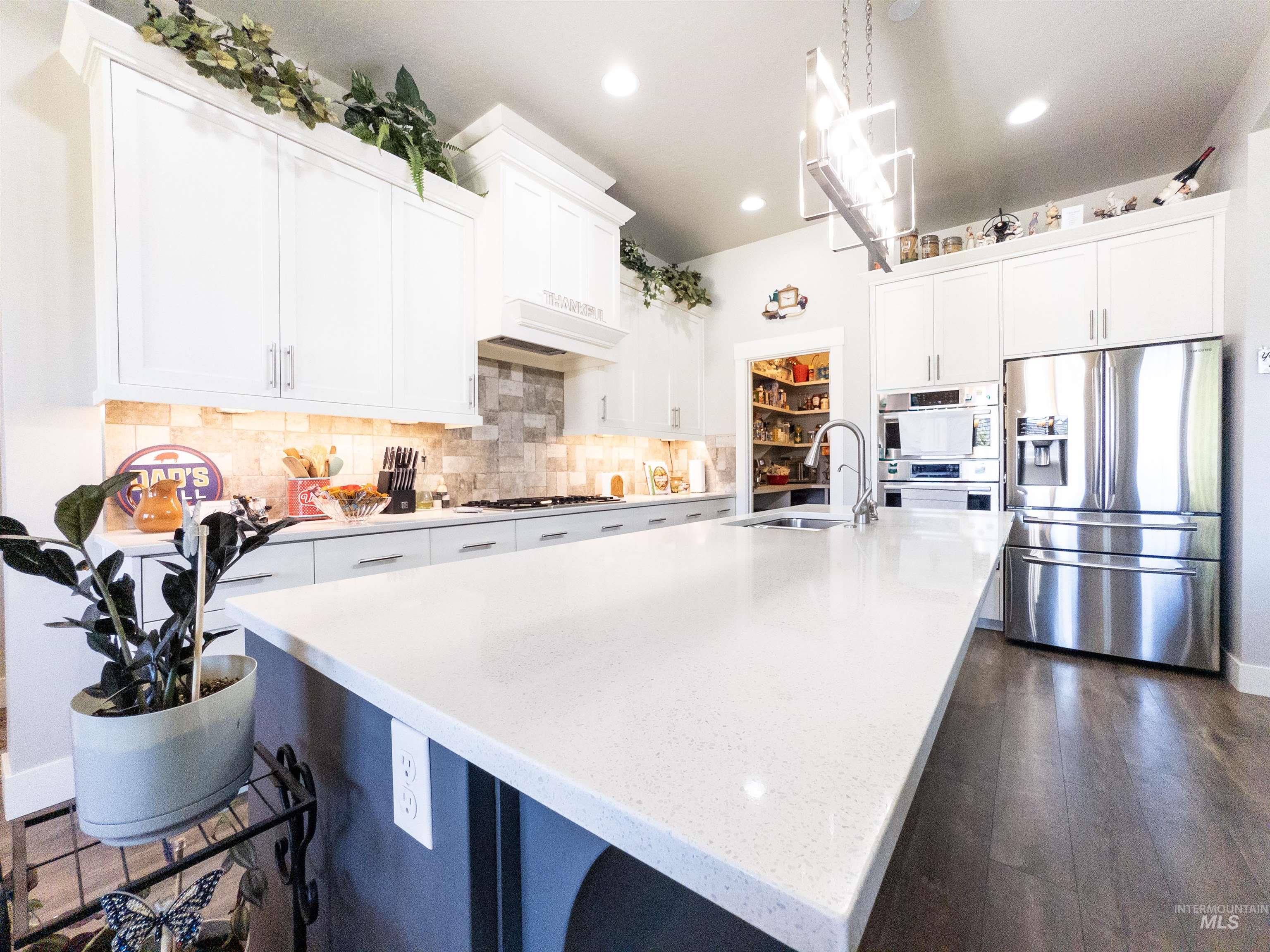 4577 North Comiso Place Meridian, ID 83646 - Photo 11 of 47 Kitchen featuring appliances with stainless steel finishes, white cabinets, tasteful backsplash, pendant lighting, and light stone counters