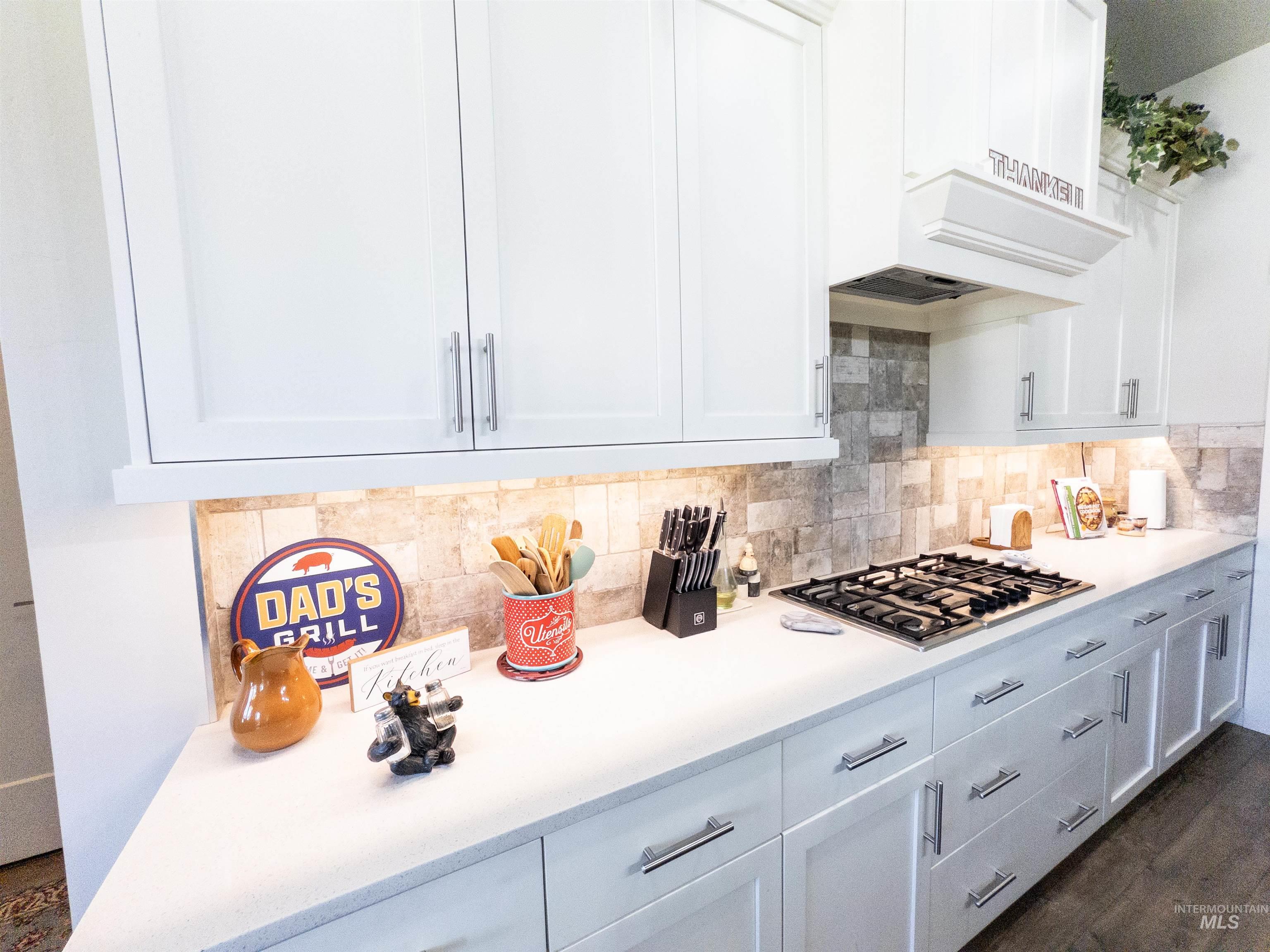 4577 North Comiso Place Meridian, ID 83646 - Photo 14 of 47 Kitchen with white cabinets, tasteful backsplash, stainless steel gas stovetop, and dark wood-style floors