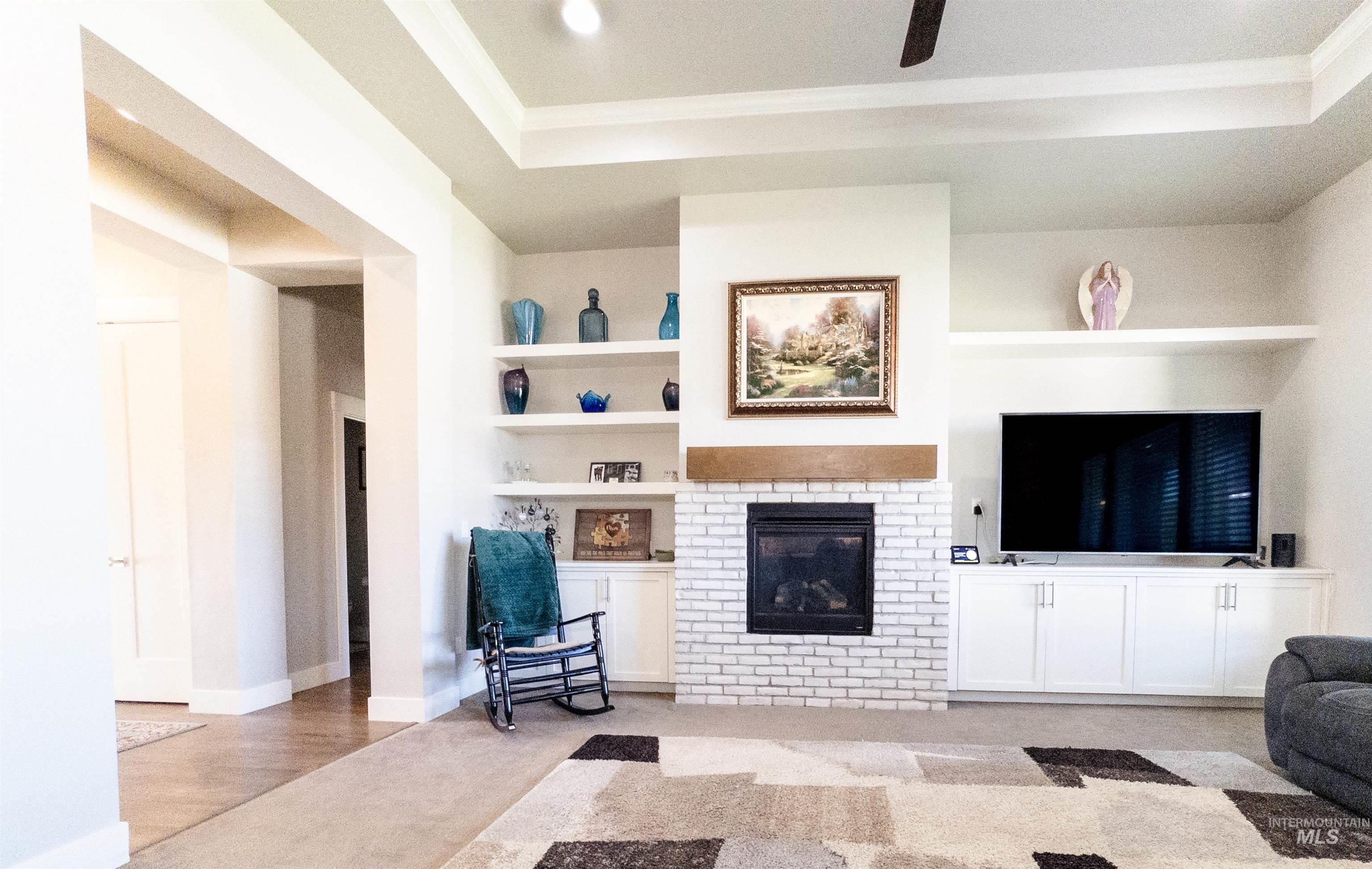 4577 North Comiso Place Meridian, ID 83646 - Photo 6 of 47 Living room with built in shelves, a fireplace, a tray ceiling, light carpet, and ornamental molding
