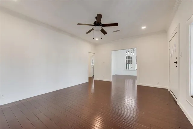 a view of an empty room with wooden floor and a ceiling fan