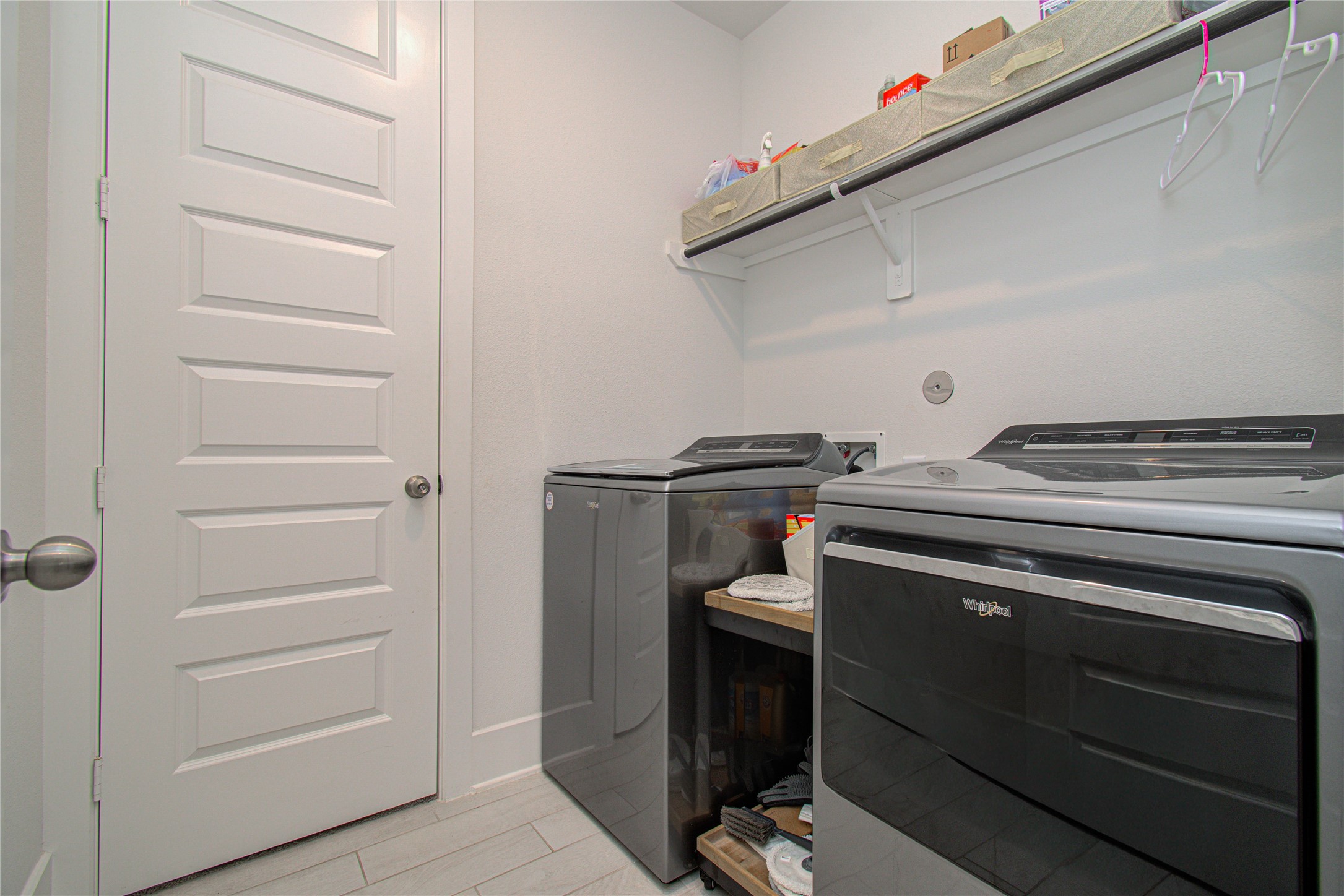 4211 Limestone Terrace Manvel, TX 77578 - Photo 30 of 33 This photo shows a modern laundry room with a sleek washer and dryer set. It features light-colored walls, a storage shelf above for organization, and a tiled floor for easy maintenance.