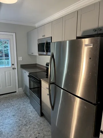 a view of a refrigerator in kitchen and an empty room with wooden floor