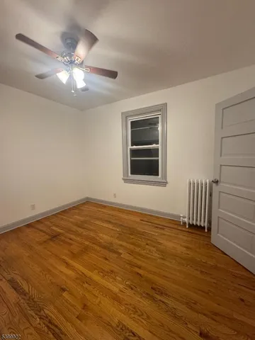 a view of an empty room with wooden floor and a ceiling fan
