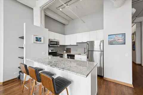 a kitchen with stainless steel appliances granite countertop a refrigerator a stove top oven a sink dishwasher and white cabinets with wooden floor