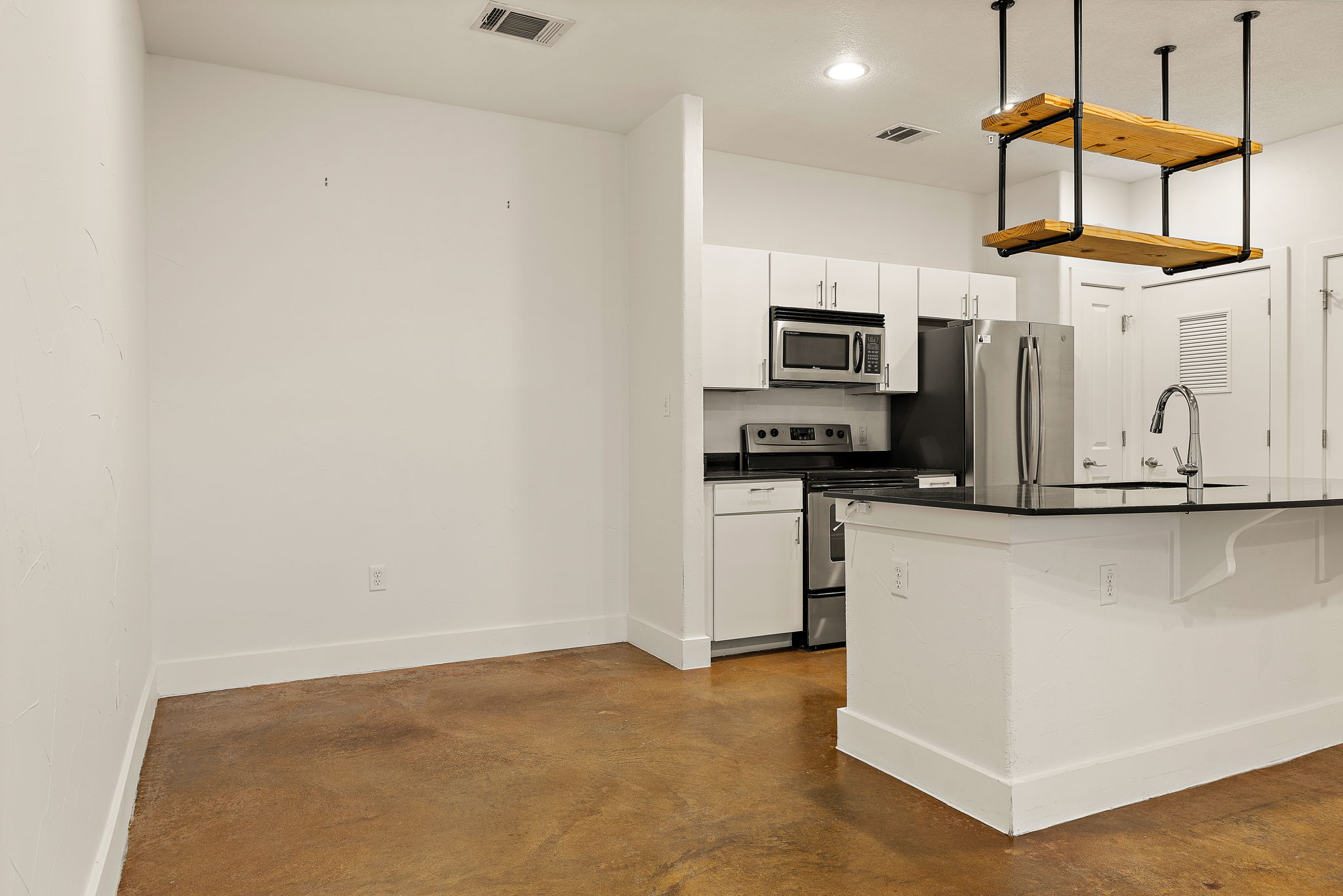 1807 Poquito Street, Unit 41 Austin, TX 78702 - Photo 15 of 23 Kitchen featuring appliances with stainless steel finishes, a breakfast bar area, white cabinetry, pendant lighting, and concrete flooring