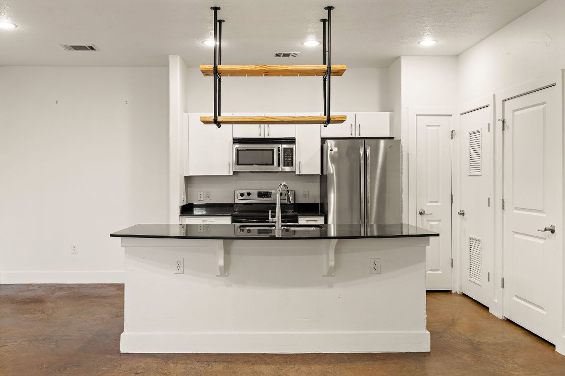 1807 Poquito Street, Unit 41 Austin, TX 78702 - Photo 9 of 23 a kitchen with stainless steel appliances granite countertop a refrigerator a stove and a sink with wooden floor