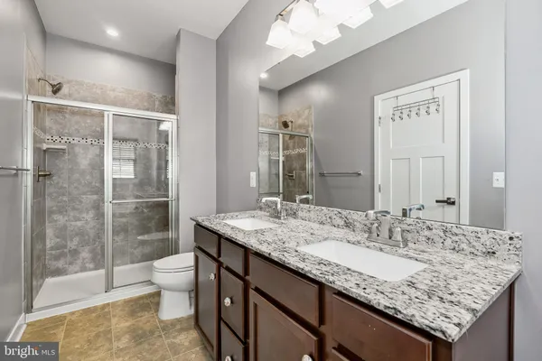 a bathroom with a granite countertop sink a toilet a mirror and shower