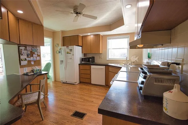 a kitchen with a refrigerator a stove top oven a sink dishwasher and white cabinets with wooden floor