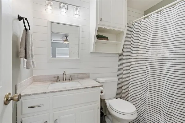 a bathroom with a granite countertop toilet a sink a mirror and shower curtain