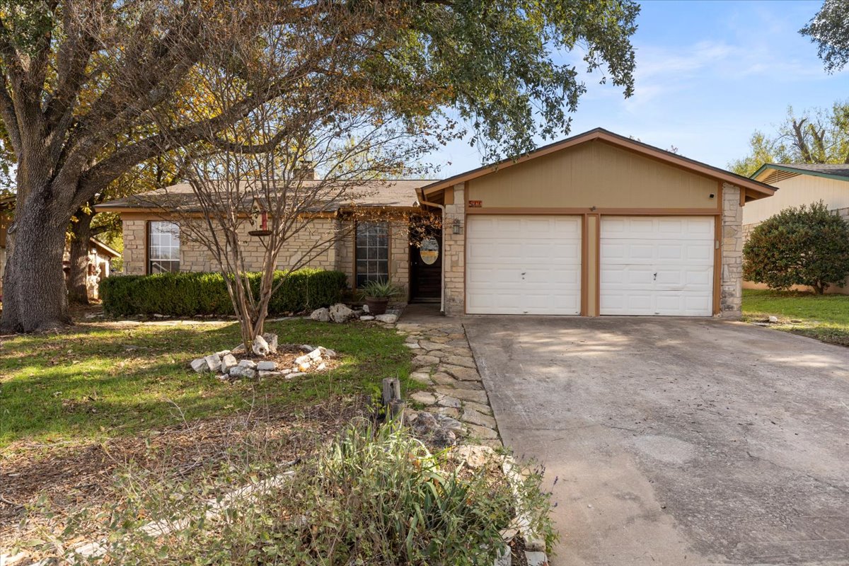 Front of house with driveway, stone siding, a front lawn, and a garage