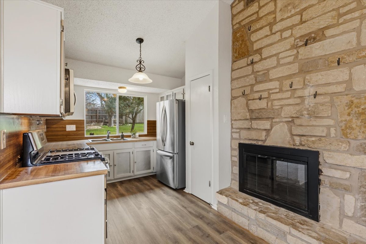 511 Suzzane Road Pflugerville, TX 78660 - Photo 12 of 35 Kitchen with white cabinetry, a fireplace, stainless steel appliances, new LVP floors, and hanging light fixtures