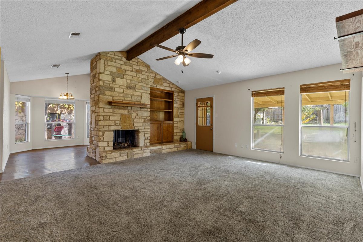 511 Suzzane Road Pflugerville, TX 78660 - Photo 5 of 37 Living room with a textured ceiling, healthy amount of natural light, a ceiling fan, a stone fireplace, and carpet flooring