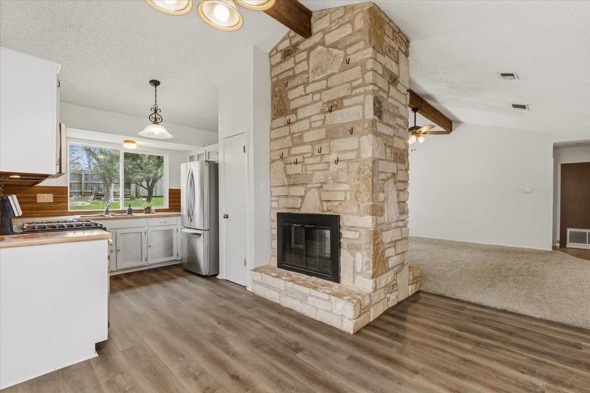 511 Suzzane Road Pflugerville, TX 78660 - Photo 9 of 35 Kitchen featuring beamed ceiling, white cabinets, a stone fireplace, hanging light fixtures, and stainless steel appliances