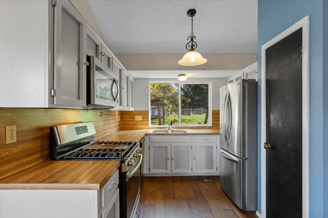 511 Suzzane Road Pflugerville, TX 78660 - Photo 10 of 34 Kitchen featuring appliances with stainless steel finishes, hanging light fixtures, light countertops, a textured ceiling, and dark wood-style floors