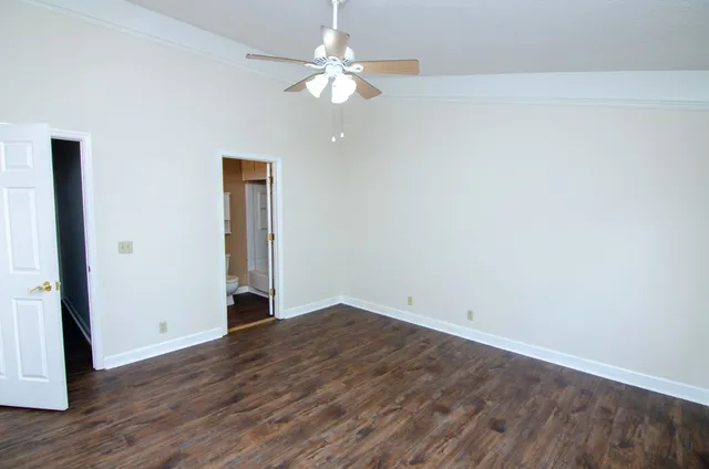 an empty room with wooden floor chandelier fan and windows