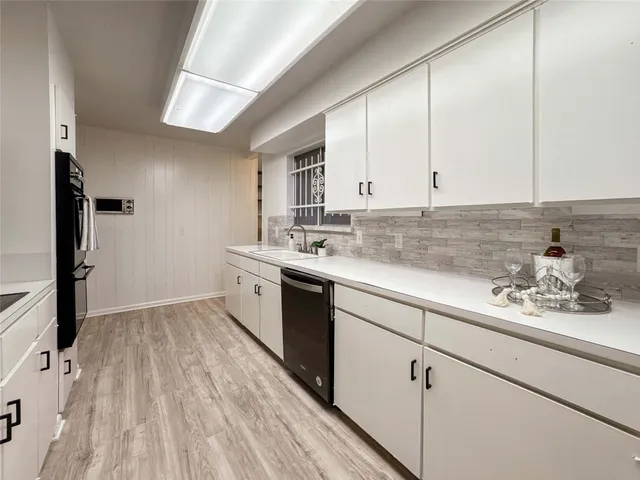 a kitchen with a sink dishwasher and white cabinets with wooden floor