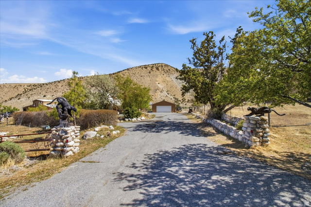 811 East Canyon Road Mayfield, UT 84643 - Photo 57 of 57 Gravel driveway entrance featuring stone pillars with decorative animal sculptures, mature trees, and a distant two-car garage with a brown exterior