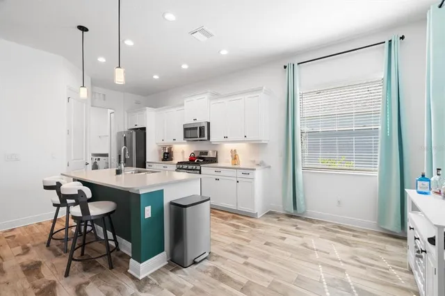 a kitchen with stainless steel appliances kitchen island granite countertop a refrigerator a stove a sink a dining table and chairs with wooden floor