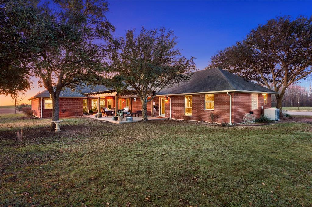 231 Trlica Road West, TX 76691 - Photo 36 of 36 Spacious backyard shaded by mature trees, creating a peaceful, private setting. A covered patio with a charming pergola provides a welcoming outdoor living space ideal for relaxing or entertaining, with plenty of room for seating and potted plants. Multiple rear entry points offer convenient access to the home, while the wide-open lawn and surrounding views enhance the property’s country feel.