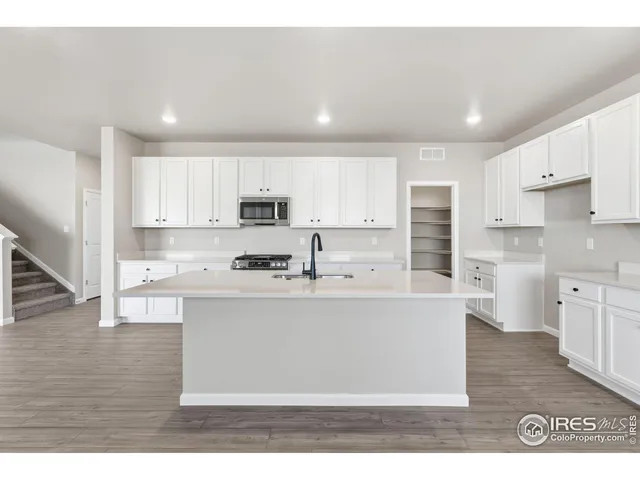 a large white kitchen with stainless steel appliances granite countertop a stove a sink a refrigerator and white cabinets