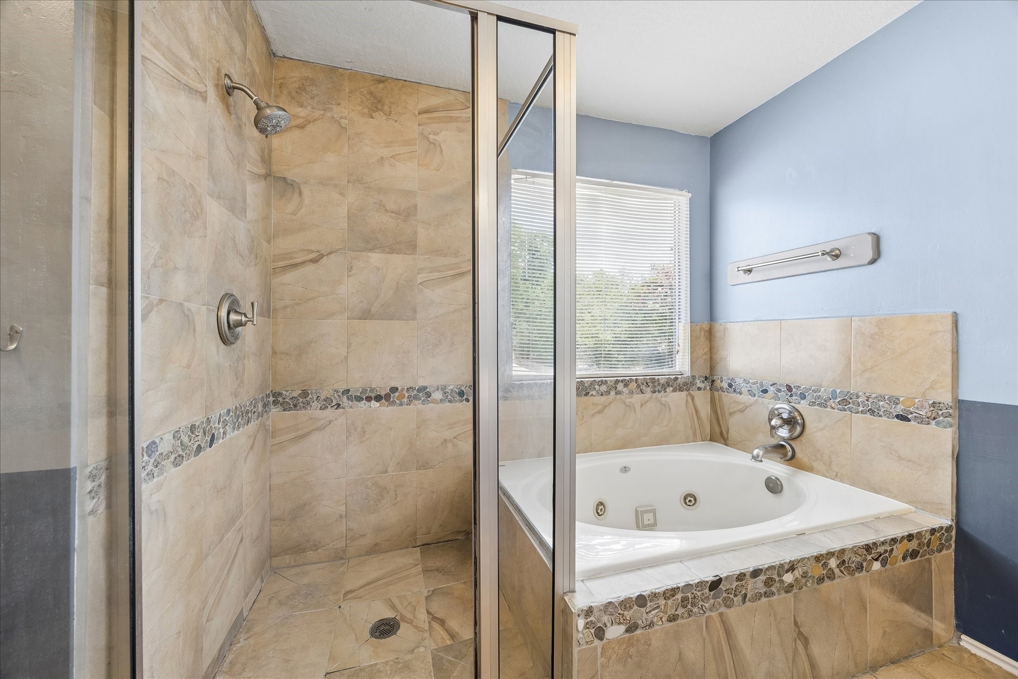 23234 Grand Rapids Lane Spring, TX 77373 - Photo 21 of 30 Spa-like jetted tub and glass-enclosed walk-in shower are finished with elegant travertine tile and a decorative pebble accent border.