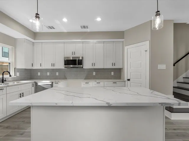 a large white kitchen with granite countertop a stove a sink a refrigerator and white cabinets with wooden floor