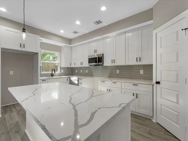 a large white kitchen with a large island oven a sink appliances and a wooden floor