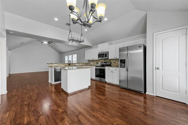 a kitchen with stainless steel appliances granite countertop a refrigerator a stove top oven a sink dishwasher and white cabinets with wooden floor