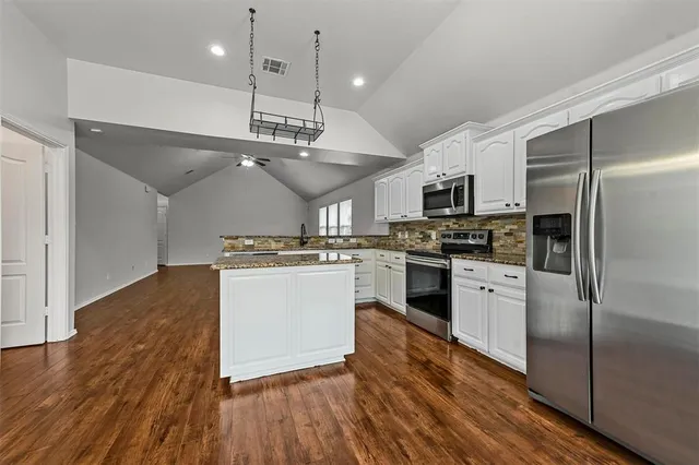 a kitchen with granite countertop a refrigerator a stove top oven a sink and cabinets