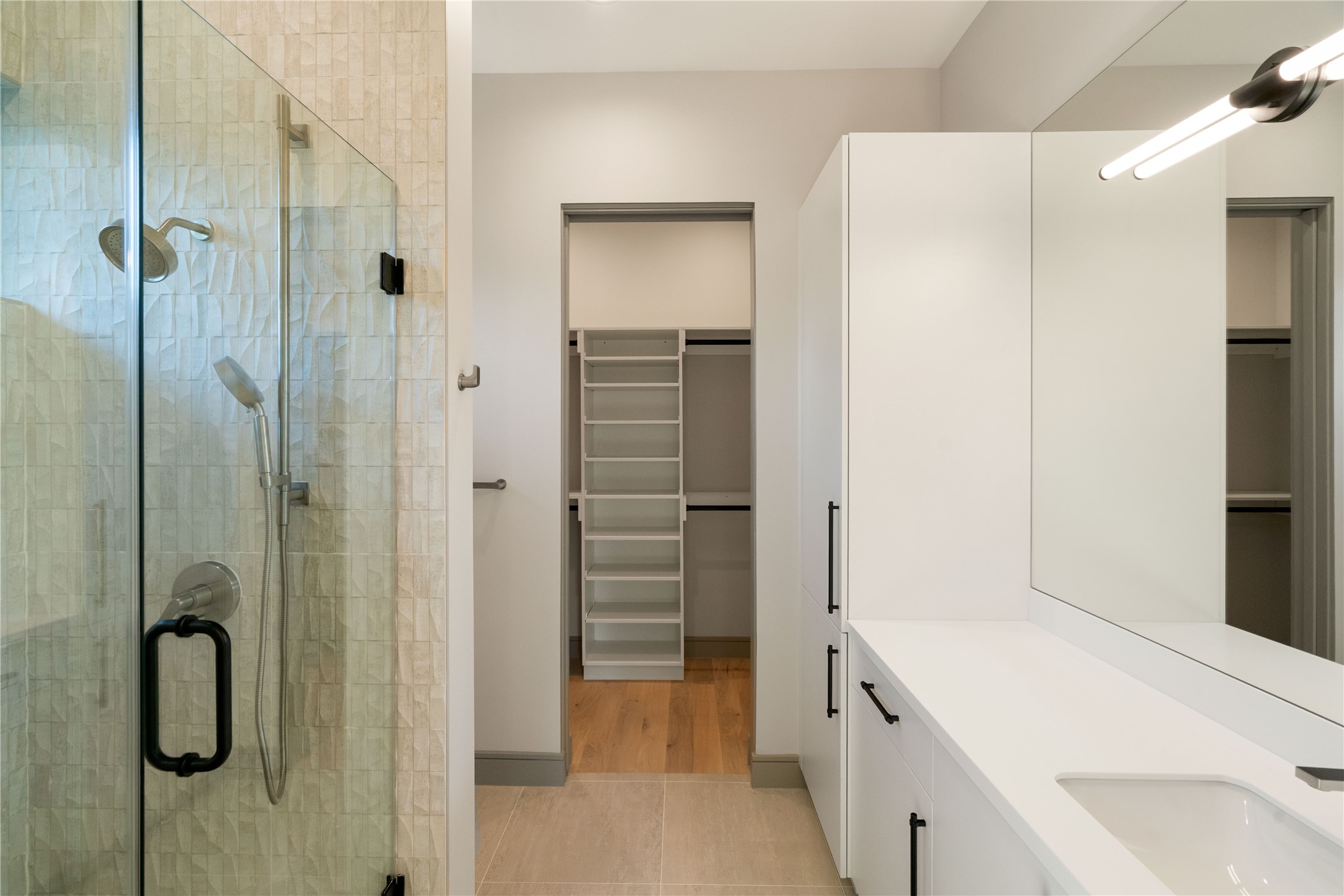 47 Pronghorn Place Spring, TX 77389 - Photo 31 of 44 This modern bathroom features a sleek glass-enclosed shower with textured tiles, a spacious vanity with clean lines, and ample storage. It leads to a walk-in closet with organized shelving, enhancing functionality and style.