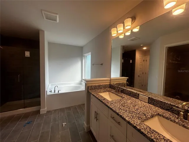 a bathroom with a granite countertop double vanity sink a mirror and shower