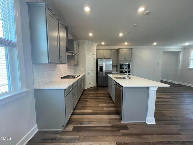 a large white kitchen with kitchen island a sink wooden floor and stainless steel appliances