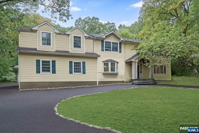 a view of a white house next to a yard with large trees