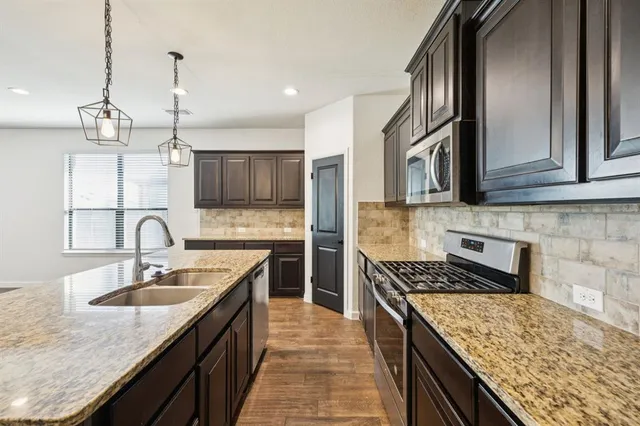 a kitchen with stainless steel appliances granite countertop a stove top oven a sink dishwasher a refrigerator and a dining table with wooden floor