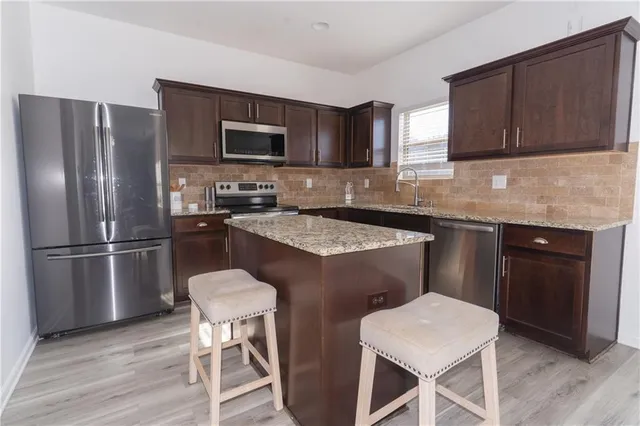 a kitchen with stainless steel appliances a sink a stove a refrigerator cabinets and dining table