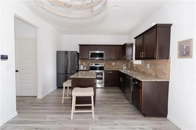 a kitchen with stainless steel appliances granite countertop a stove a sink dishwasher a refrigerator and a microwave oven with wooden floor