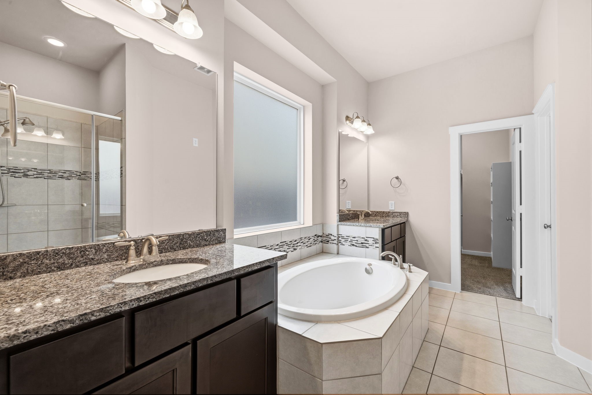 17019 Seminole Ridge Drive Cypress, TX 77433 - Photo 20 of 48 Spacious primary bath featuring dual vanities with granite countertops, a relaxing soaking tub, and a separate glass-enclosed shower. Large frosted window provides natural light while maintaining privacy.