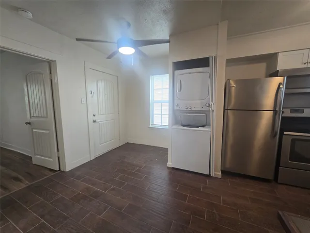 a view of a refrigerator in kitchen and an empty room with wooden floor windows