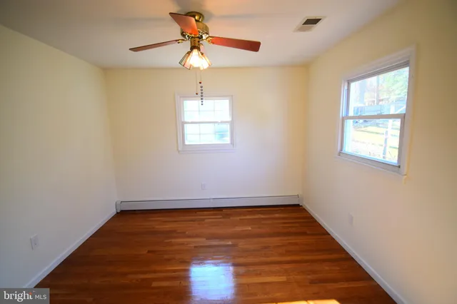 an empty room with wooden floor chandelier fan and windows