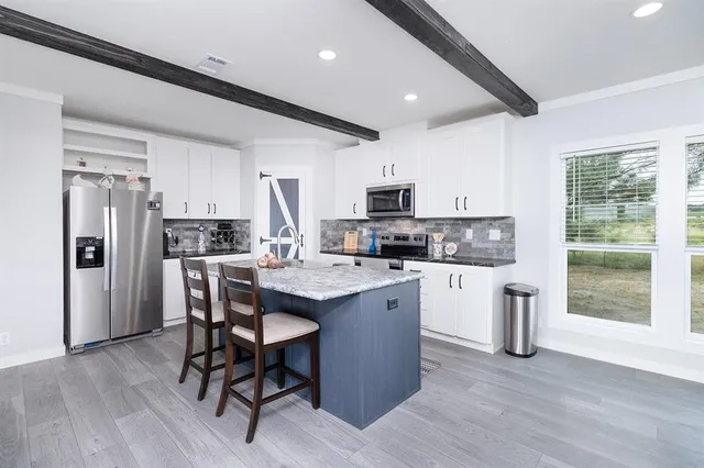 a kitchen with stainless steel appliances a microwave a sink a stove a refrigerator cabinets and dining table