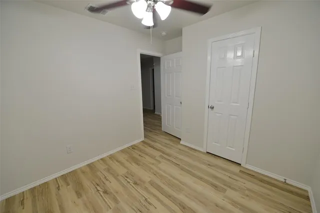 a view of an empty room with wooden floor and a chandelier fan