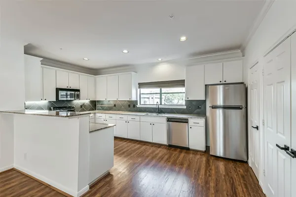 a kitchen with stainless steel appliances granite countertop a refrigerator a sink dishwasher a stove and white countertops with wooden floor