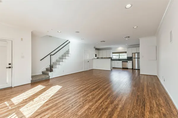a view of empty room with wooden floor and kitchen