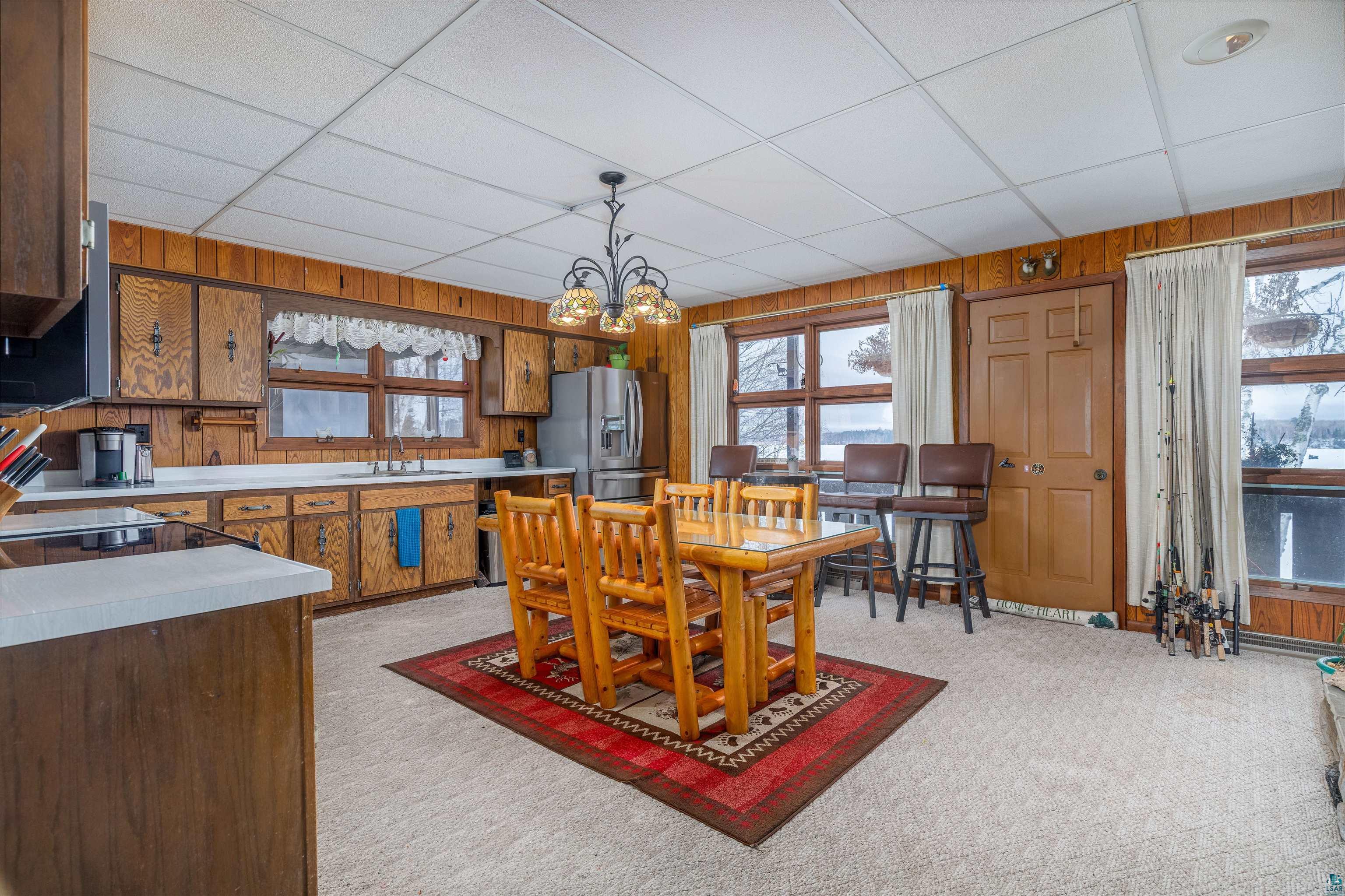 2641 Priest Point Road Ely, MN 55731 - Photo 11 of 38 Dining room featuring wooden walls, light colored carpet, plenty of natural light, a chandelier, and a drop ceiling