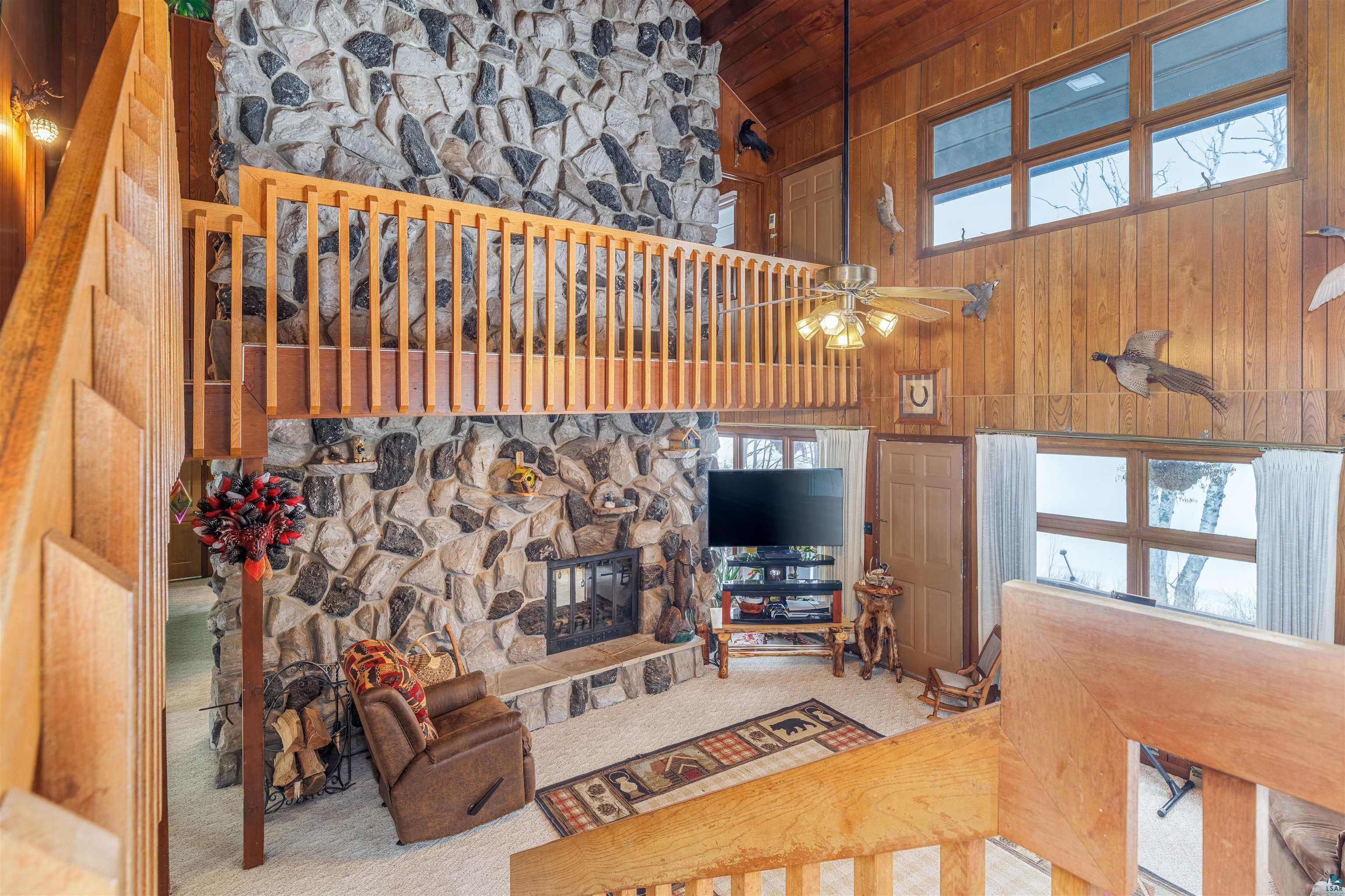 2641 Priest Point Road Ely, MN 55731 - Photo 13 of 38 Living area with a fireplace, a vaulted wooden ceiling, carpet flooring, wooden walls, and a ceiling fan
