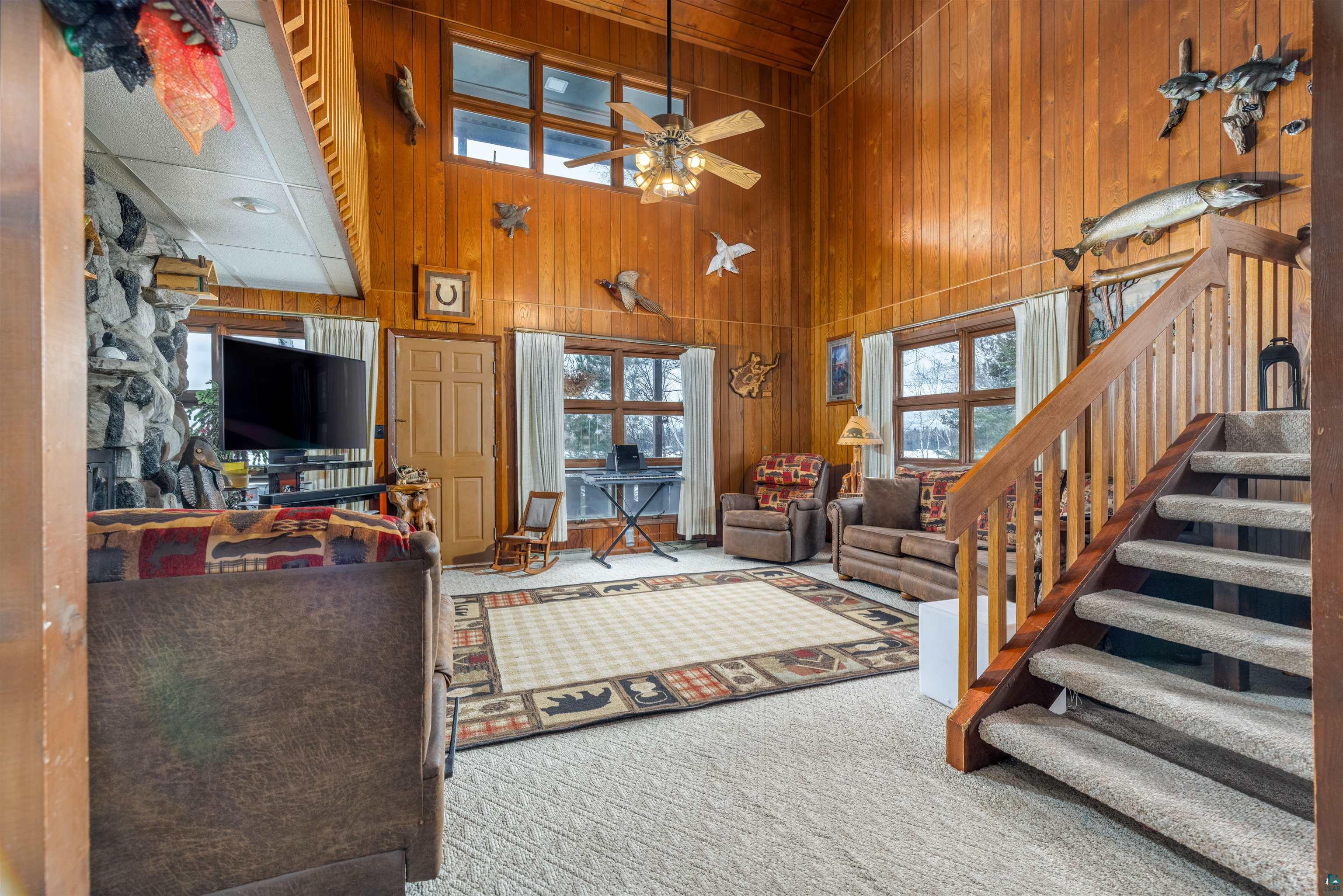 2641 Priest Point Road Ely, MN 55731 - Photo 16 of 38 Living area with wood walls, a high ceiling, light colored carpet, and a ceiling fan
