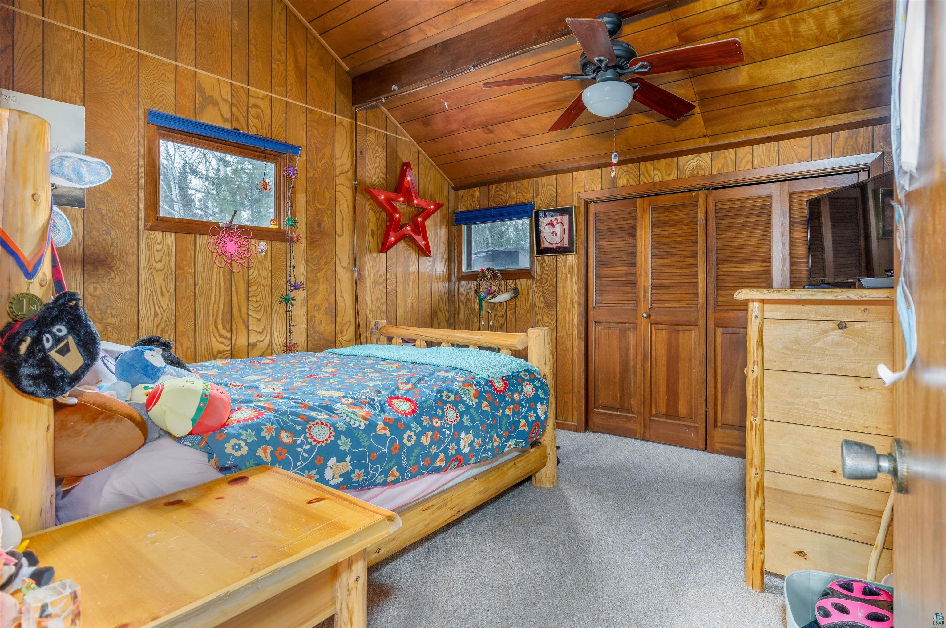 2641 Priest Point Road Ely, MN 55731 - Photo 25 of 38 Bedroom featuring vaulted ceiling with beams, light colored carpet, wooden walls, ceiling fan, and a closet